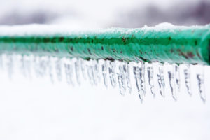 Green pipe frozen with small icicles hanging down along it.