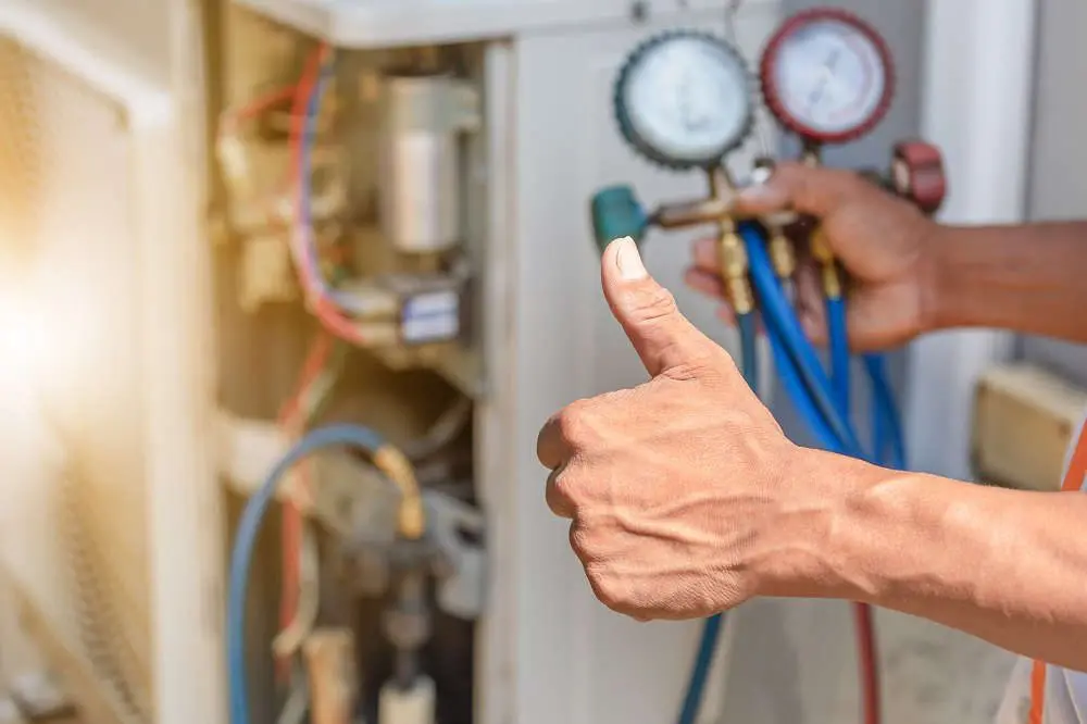 Person's hand giving a thumbs up, while other hand holds an HVAC system gauge in background.