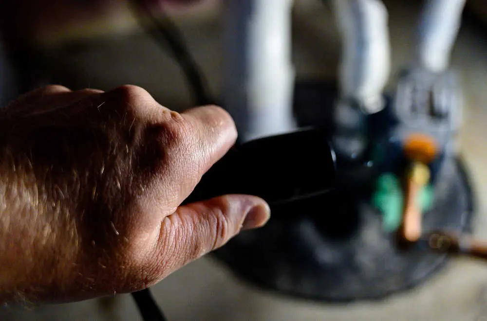 Close-up of a plumber's hand holding onto a piece of a sump pump, blurred in background.