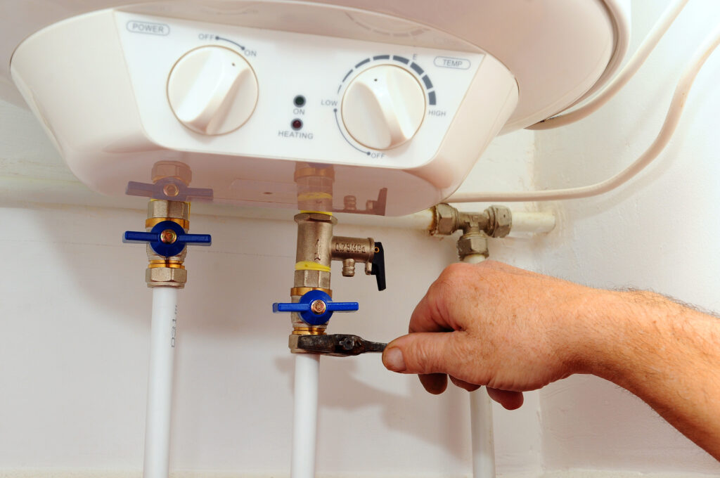 Plumber's hand adjusting pipes on the bottom of a tankless water heater.