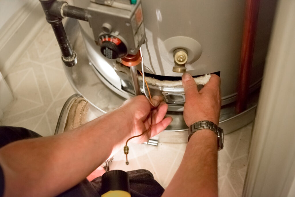 Close view of a plumber's hands as they remove the access panel on a tank water heater to perform maintenance.