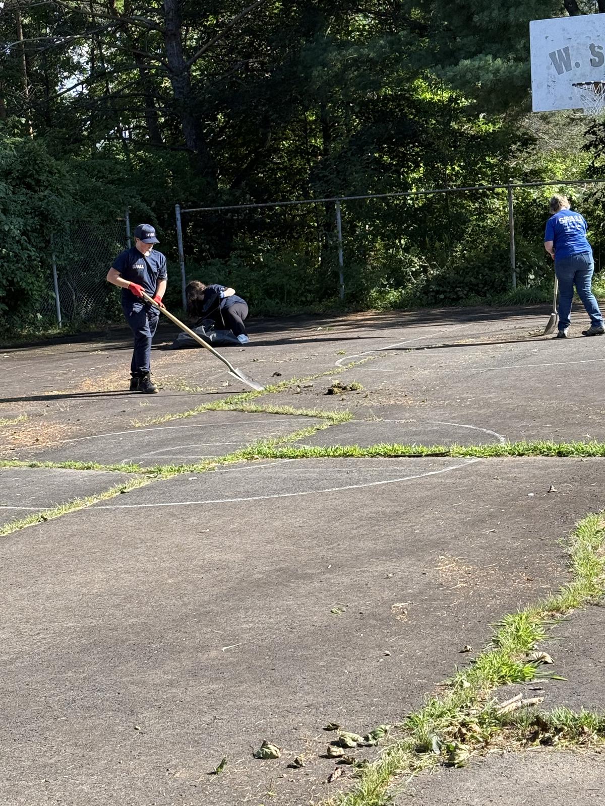 Volunteers scraping grass and weeds out of the cracks in the basketball court.