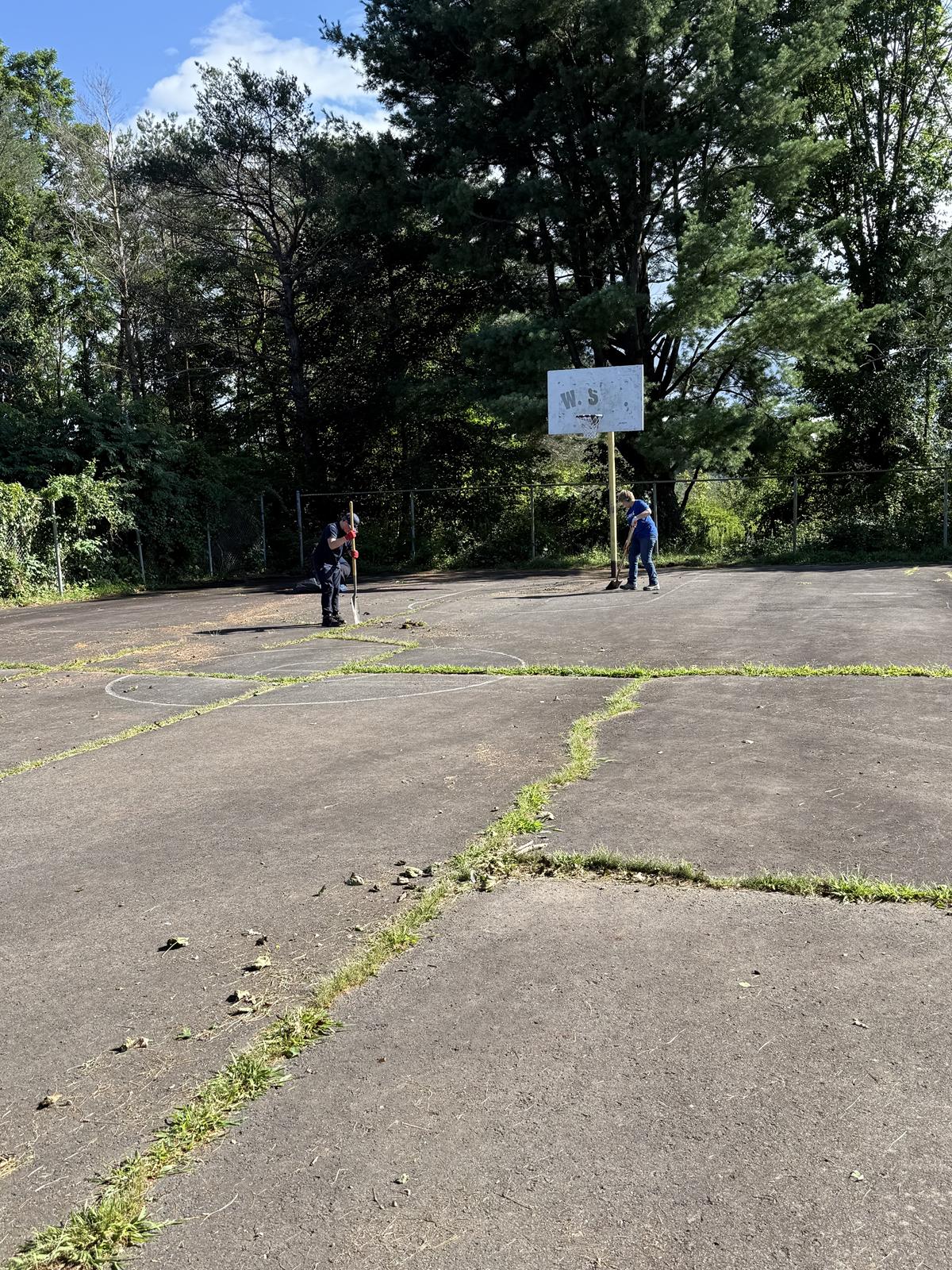 Two volunteers working with shovels on the Cerra Park basketball court.