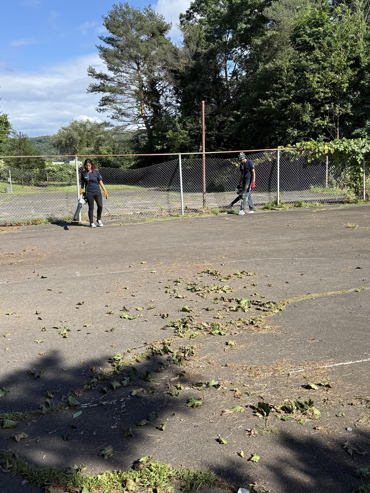 Volunteers using leaf blowers to clear cuttings off the court surface.