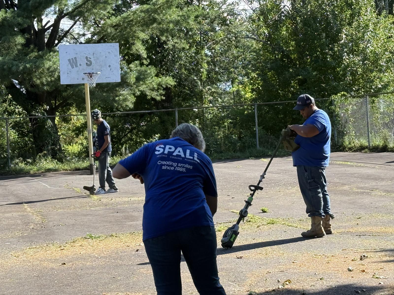 Volunteers running string trimmers near the basketball hoop at Cerra Park.
