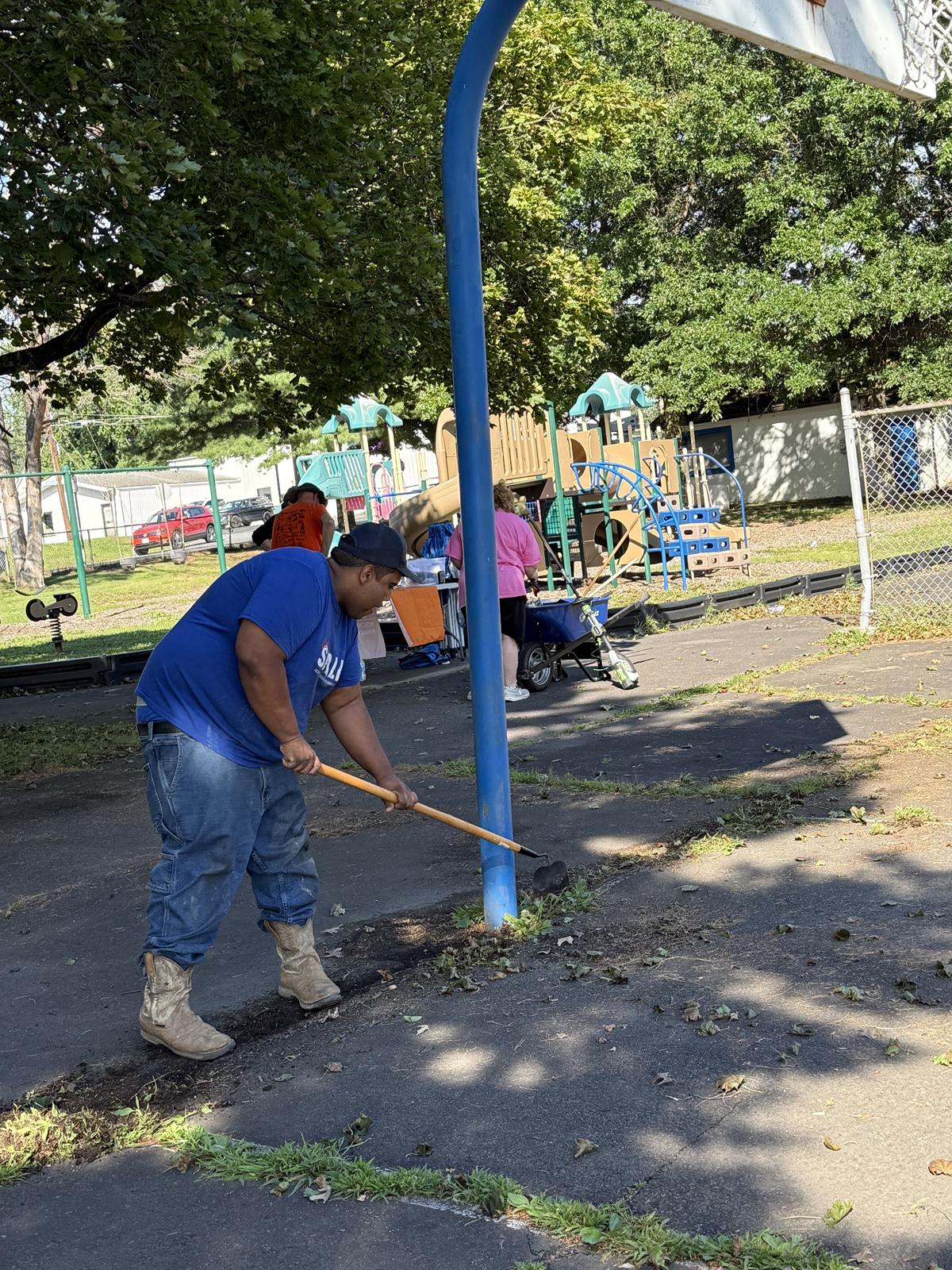 A T.E. Spall & Son team member in a company shirt clearing weeds beside the basketball court at Cerra Park.